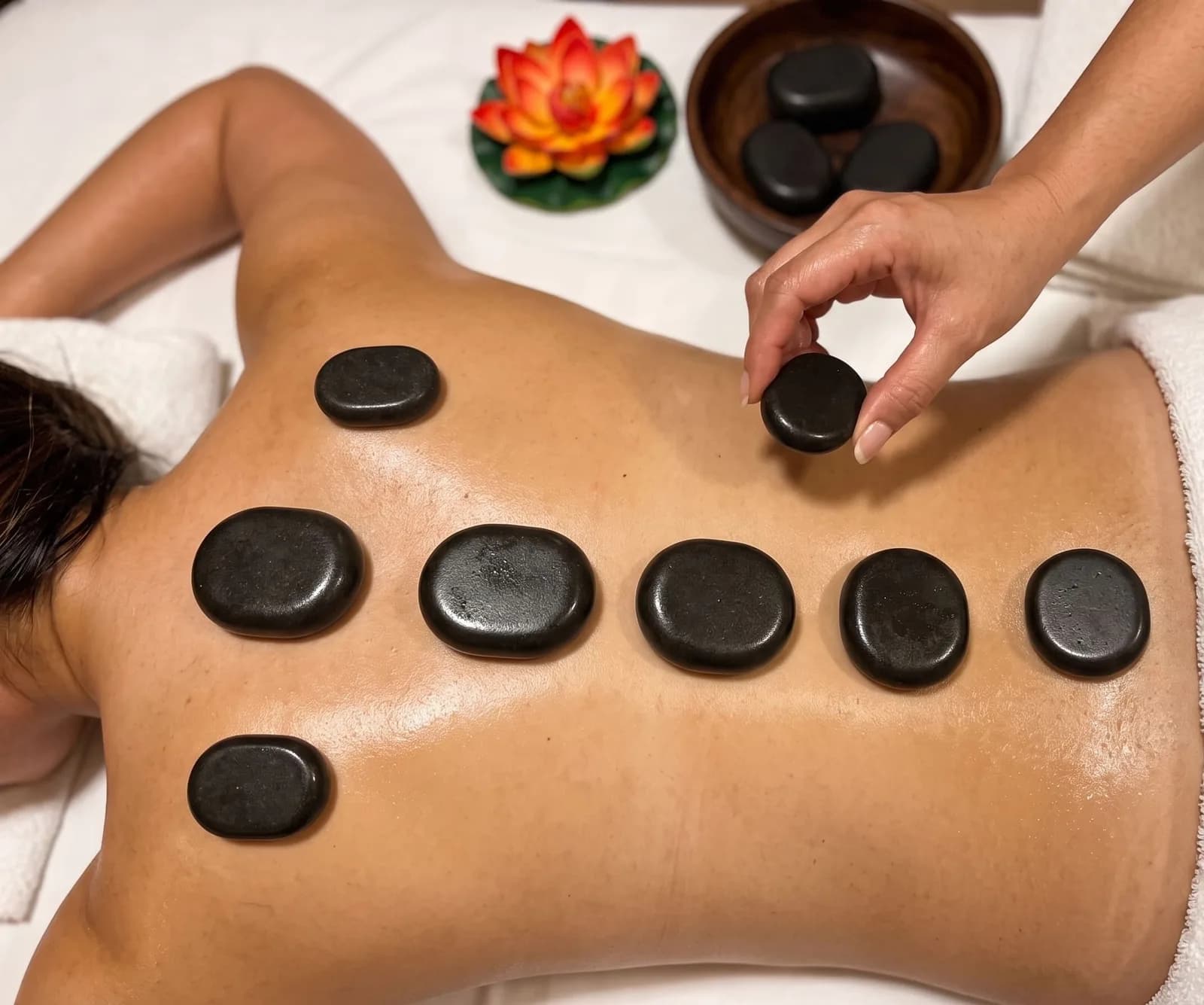 Hot Stone Massage bei BANN Thaimassage in Basel Hot Stone Massage in Basel: warme Basaltsteine auf dem Rücken, eine Masseurin legt einen Stein auf