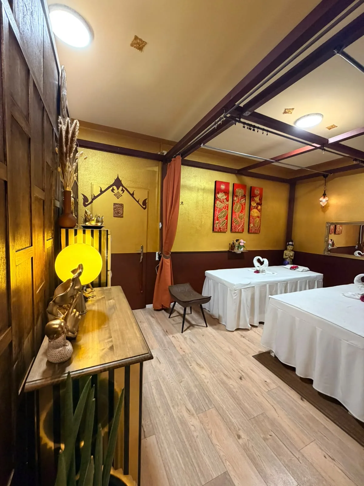 Paarraum mit goldgelben Wänden bei BANN Thaimassage Paarraum bei BANN Thaimassage in Basel mit goldgelben Wänden, roten Lotusbildern und zwei Massageliegen mit Handtuch-Schwänen