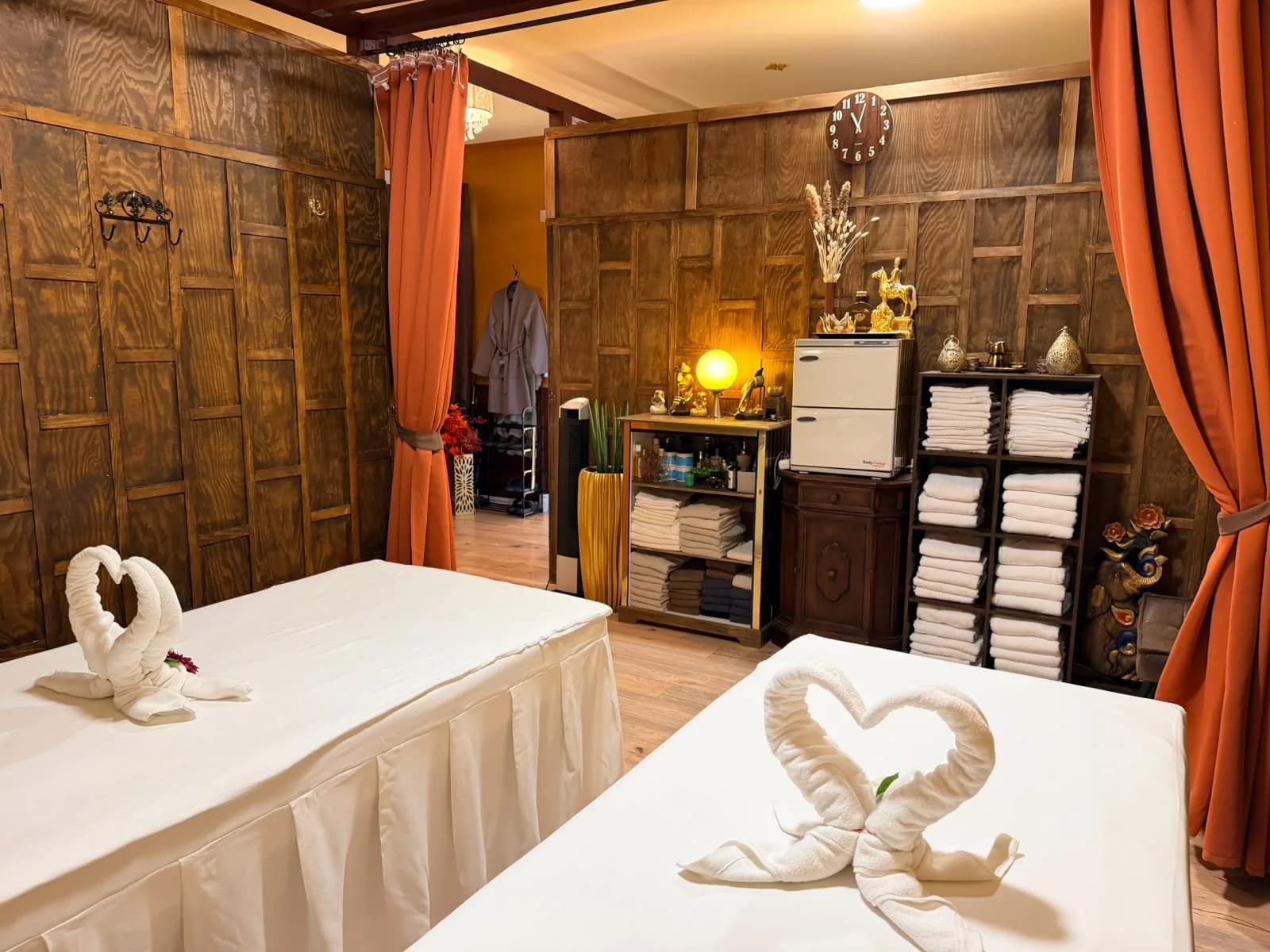 Paarraum mit Handtuch-Schwänen bei BANN Thaimassage Paarraum bei BANN Thaimassage in Basel: zwei Massageliegen mit Handtuch-Schwänen in Herzform, Holzwände und orange Vorhänge